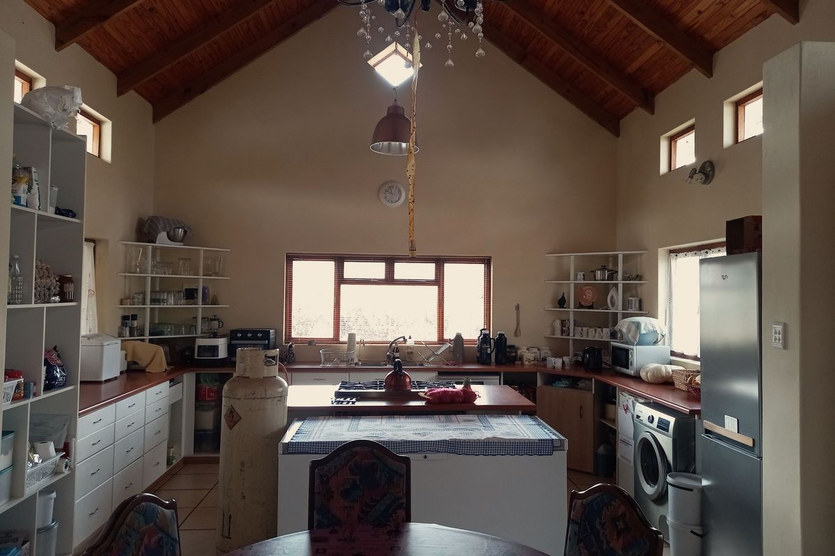 Spacious kitchen featuring a high vaulted timber ceiling, central island with integrated hob, ample counter space, and open shelving storage.