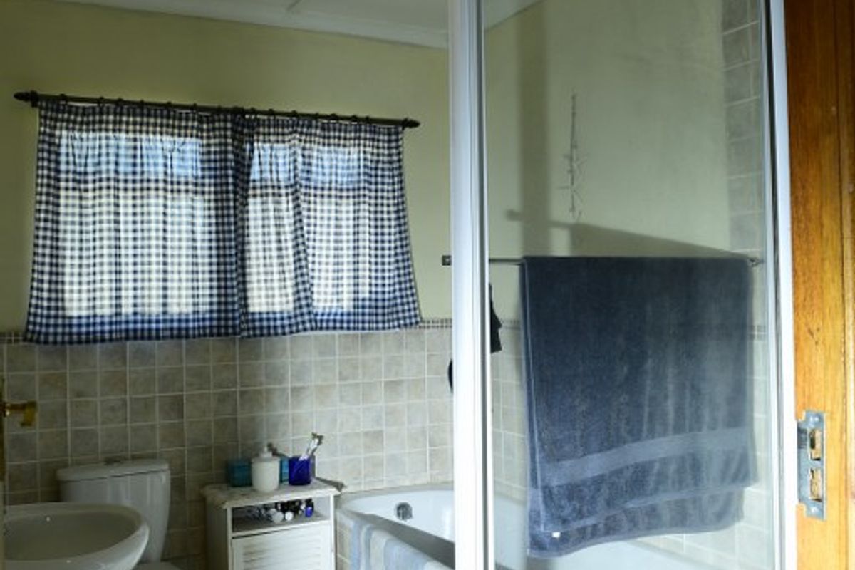 A functional bathroom featuring a pedestal basin, toilet, built-in bathtub with shower screen, and a ceiling-mounted heat lamp.