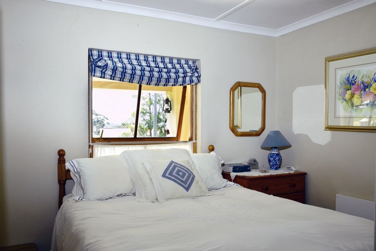 A cozy bedroom featuring a window with a view, neutral wall tones, and classic ceiling cornicing.