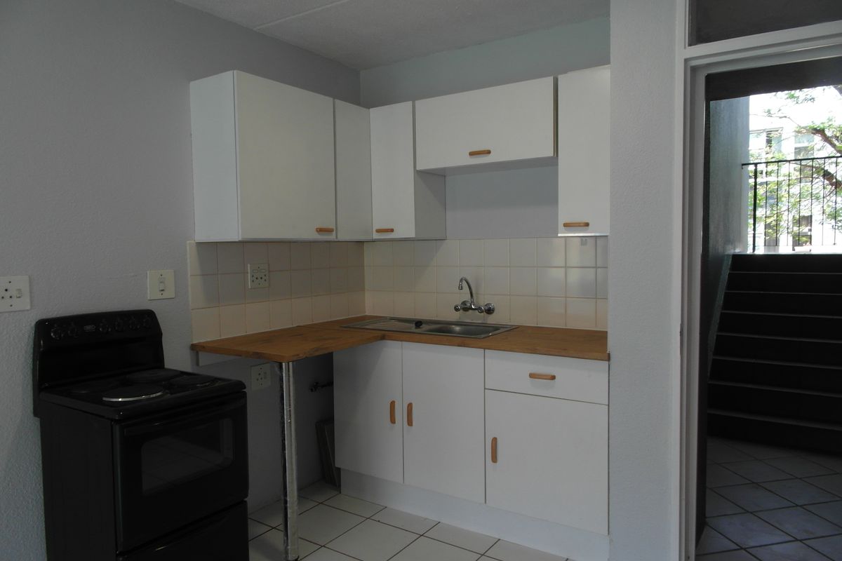 A compact kitchen featuring white cabinetry, a laminate countertop, stainless steel sink, tiled backsplash, and a freestanding stove.