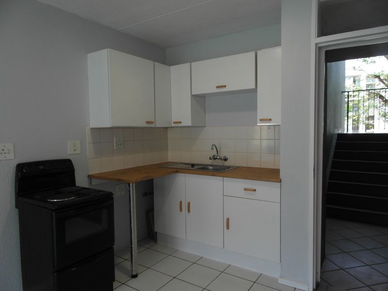 A compact kitchen featuring white cabinetry, a laminate countertop, stainless steel sink, tiled backsplash, and a freestanding stove.