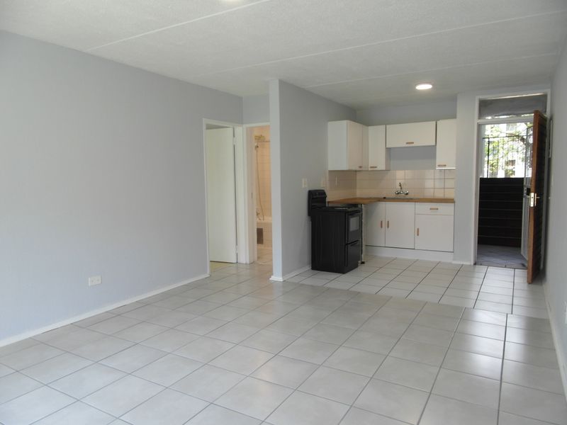 An open-plan living and kitchen area featuring tiled flooring, neutral walls, and a functional kitchen layout with built-in cabinetry and a stove.