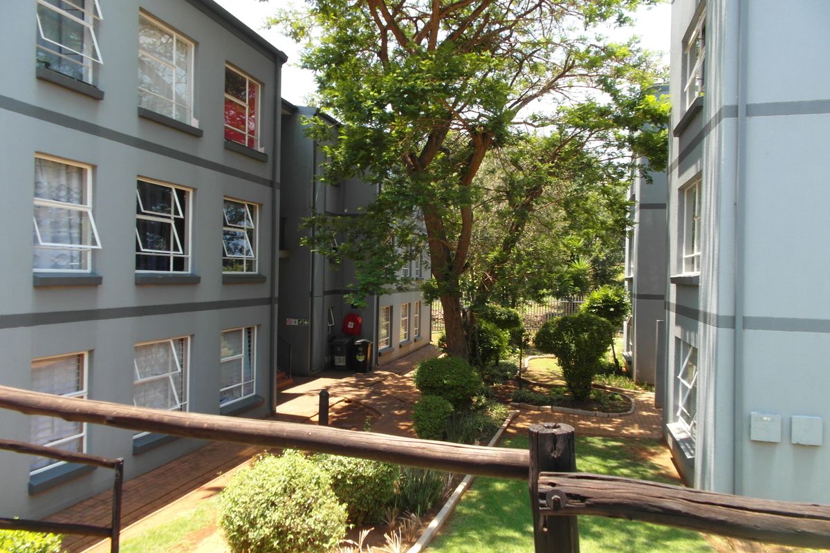 View of the apartment complex rear courtyard featuring paved walkways, landscaped garden areas, and multi-story building facades with casement windows.