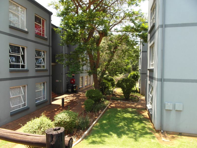 A view of the apartment complex rear courtyard featuring paved walkways, landscaped garden areas, and multi-story building facades with casement windows.
