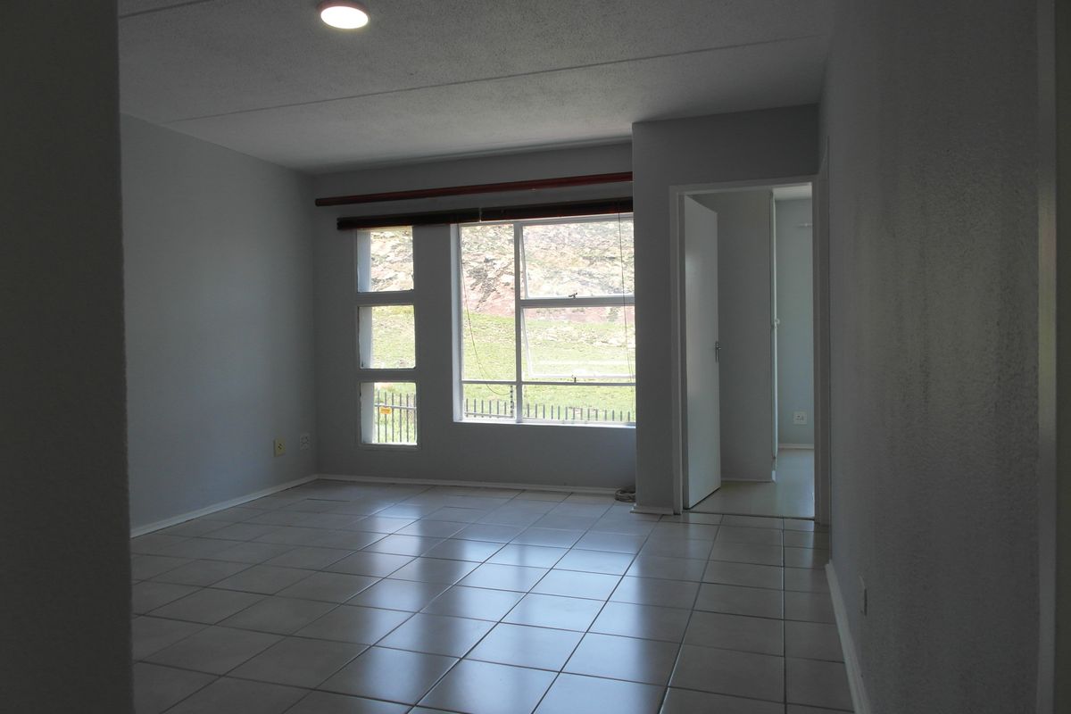 An empty living room featuring neutral tiled flooring, large aluminium-framed windows, and a clean, minimalist aesthetic ready for personalization.