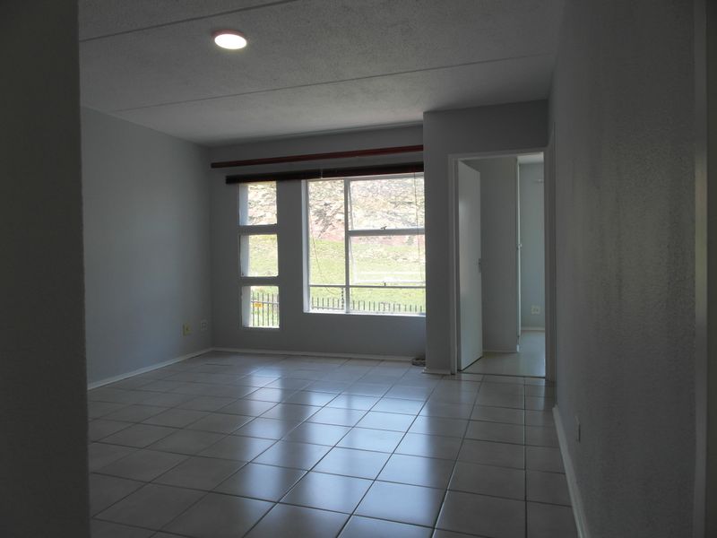An empty living room featuring neutral tiled flooring, large aluminium-framed windows, and a clean, minimalist aesthetic ready for personalization.