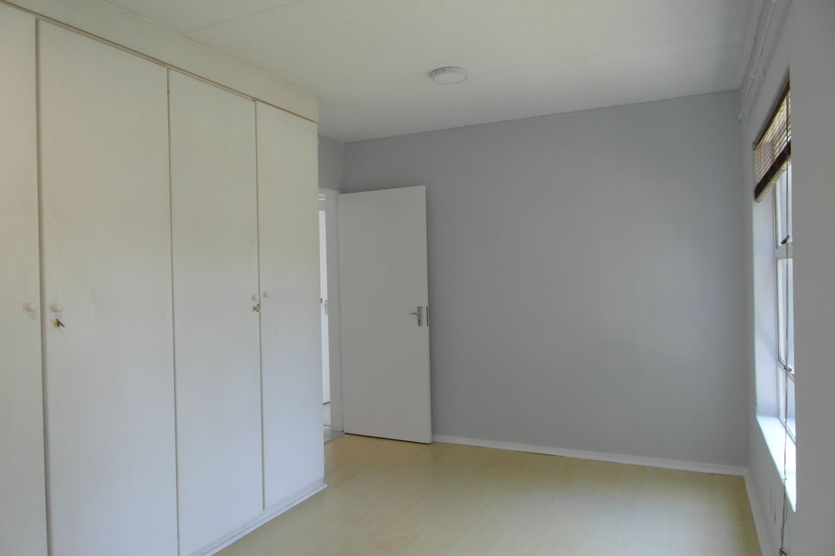 A bright, empty bedroom featuring light-toned laminate flooring and ample built-in cupboard storage space.
