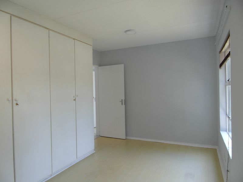 A bright, empty bedroom featuring light-toned laminate flooring and ample built-in cupboard storage space.