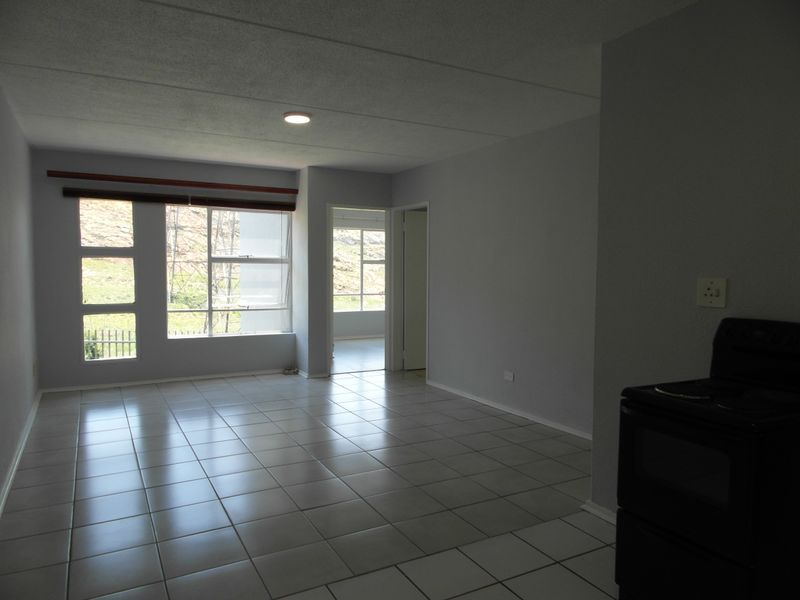 An open-plan living area featuring neutral tiled flooring, recessed lighting, and large windows that provide natural light and views.