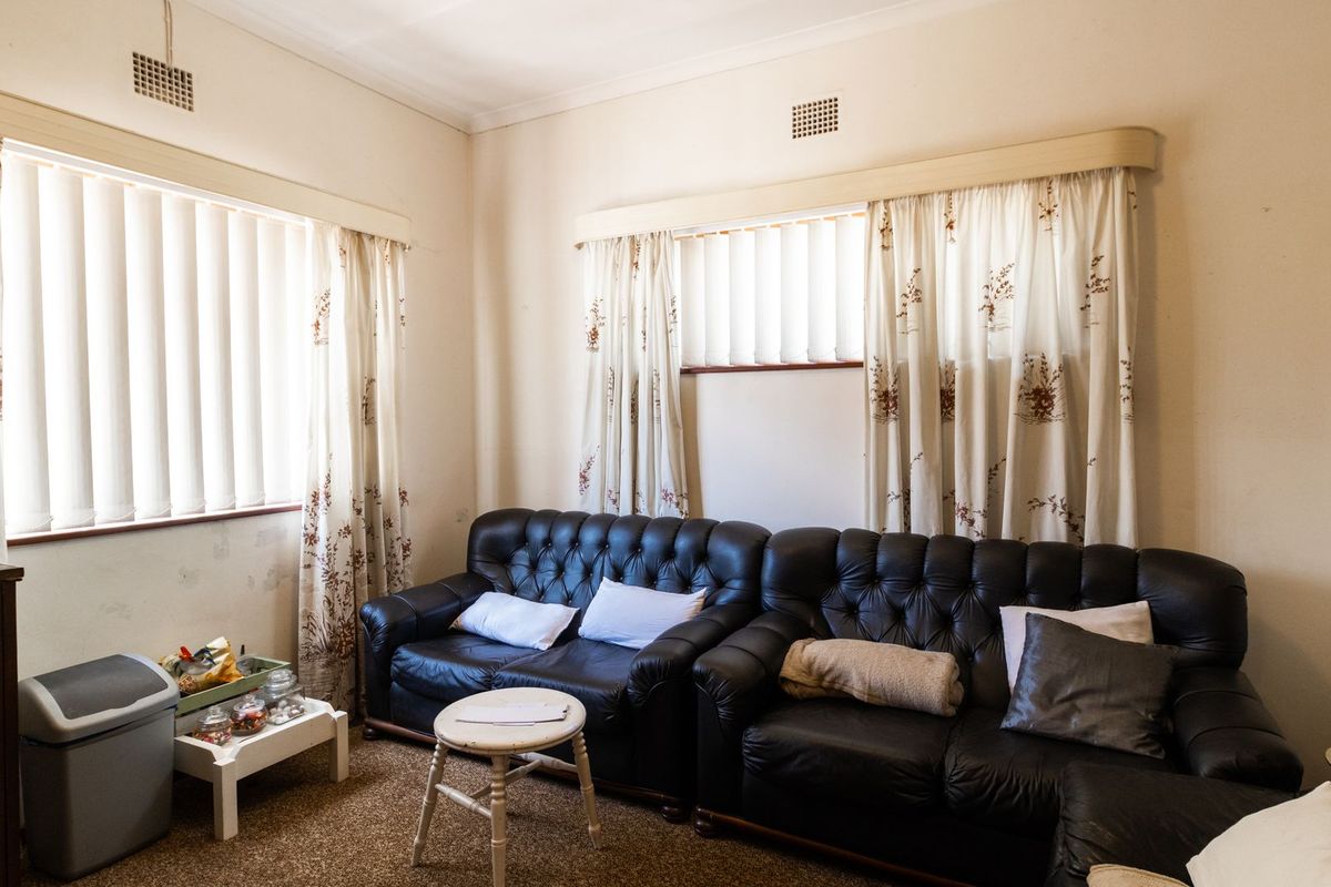 A living room featuring carpeted flooring, dual windows with vertical blinds, and ceiling ventilation grilles.