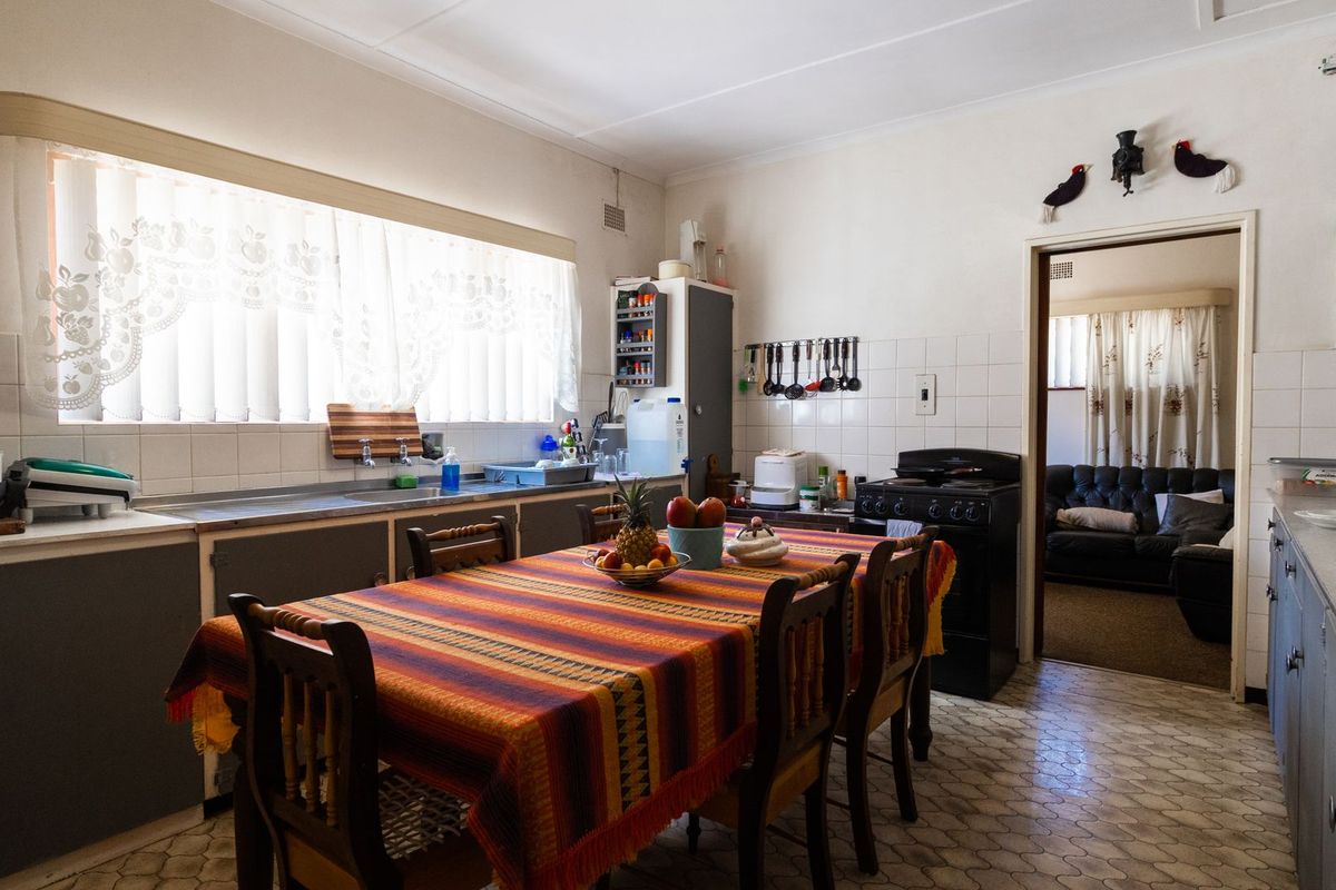 A dated kitchen featuring original cabinetry, tiled splashbacks, and a dedicated dining area with direct access to the adjacent living room.