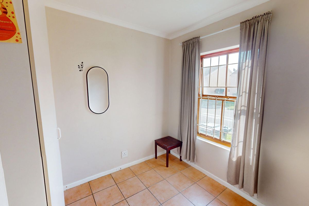 A compact bedroom featuring tiled flooring, a window with security bars, and neutral wall finishes.