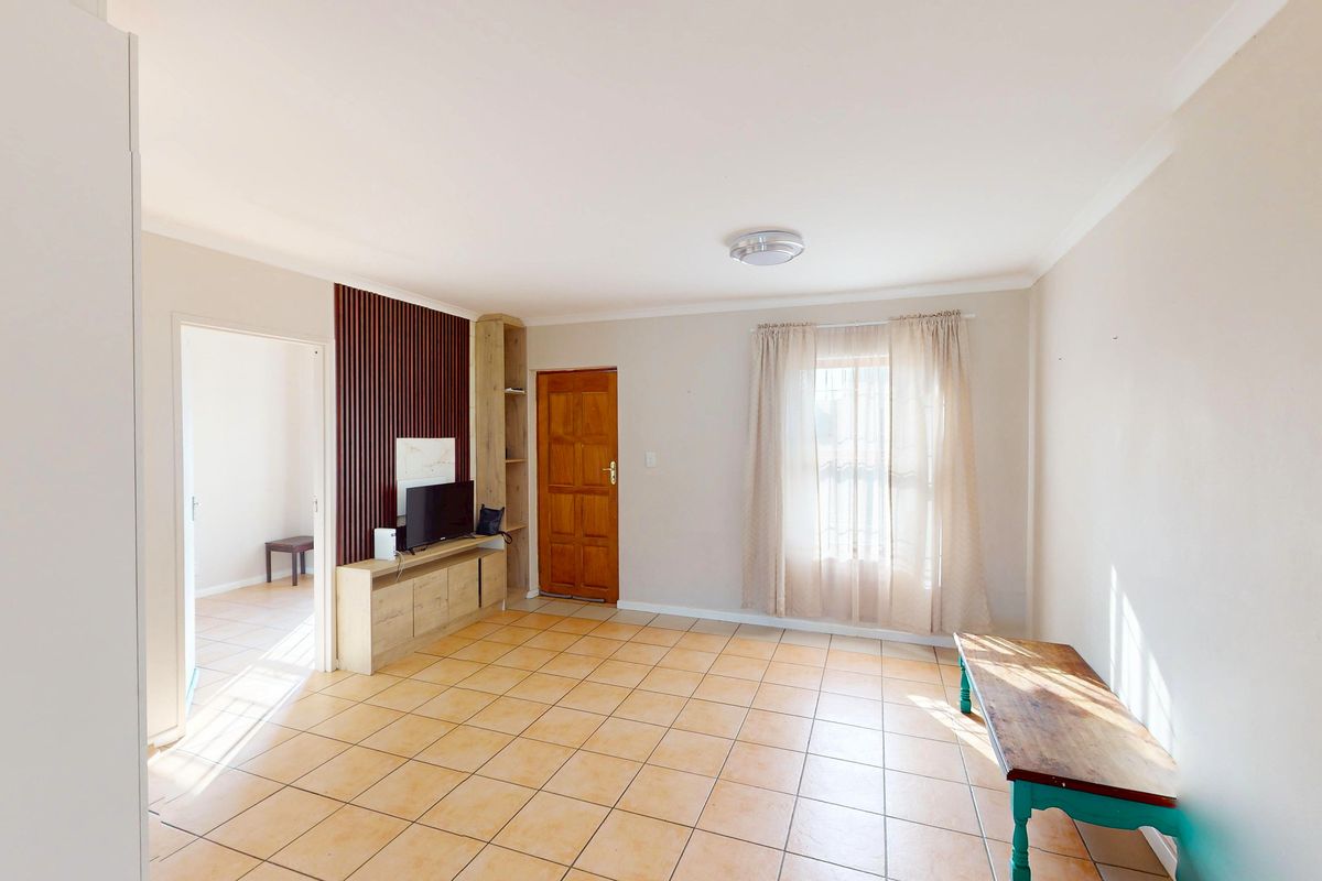 A bright living room featuring tiled flooring, a built-in wooden media unit with slat wall detailing, and a solid wood entrance door.