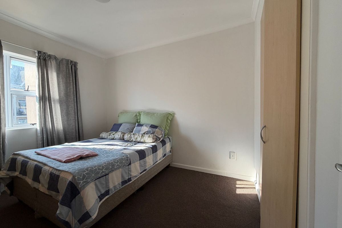 A functional bedroom featuring neutral walls, carpeted flooring, and a built-in wardrobe with light wood-finish doors.