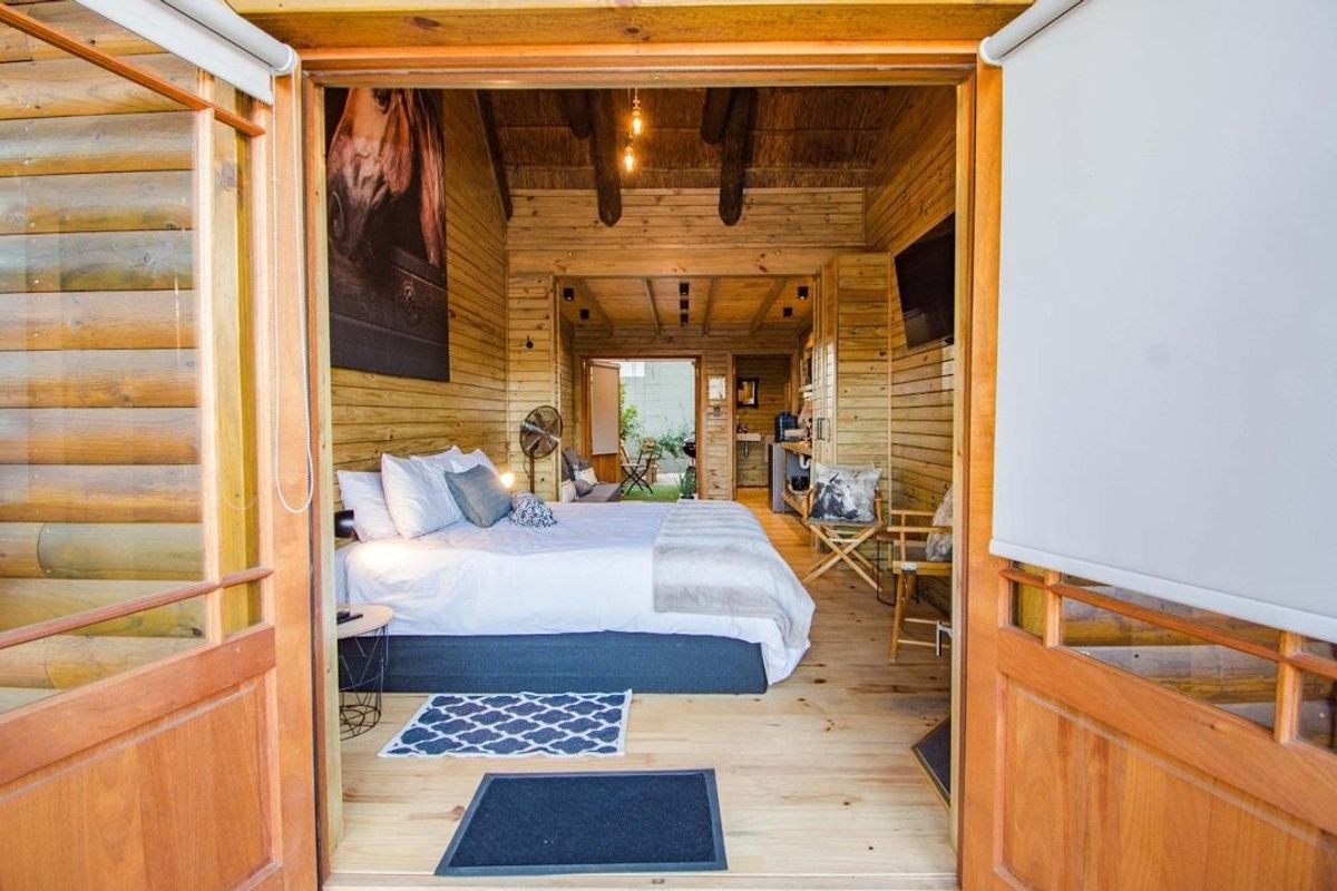 A cozy bedroom featuring exposed timber log walls and ceiling beams, with integrated kitchenette and direct access to an outdoor patio area.