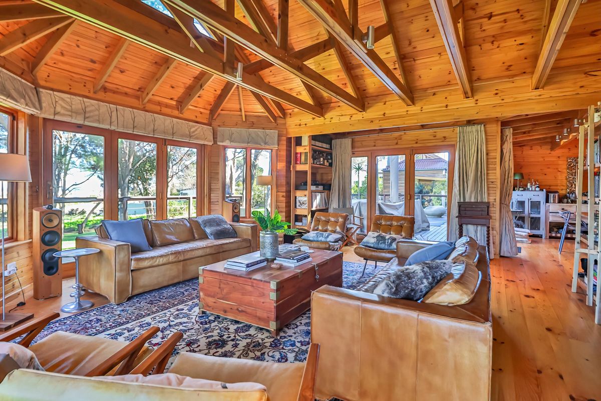 Spacious living room featuring high exposed timber vaulted ceilings, warm wood wall paneling, polished timber floors, and extensive glass doors opening to the outdoors.