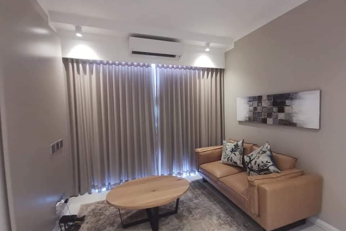 A modern living room featuring a wall-mounted air conditioning unit, recessed ceiling spotlights, and floor-to-ceiling curtains.
