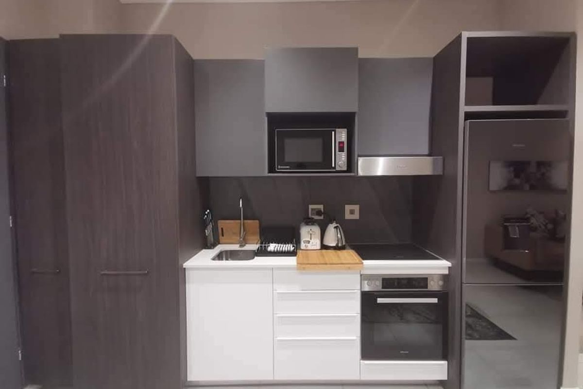 Modern compact kitchen featuring dark wood-grain cabinetry, white stone countertops, built-in oven, electric hob, extractor fan, and integrated microwave.