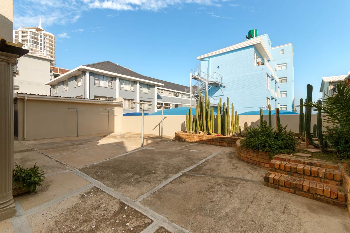 A paved rear courtyard area featuring brick retaining walls, established cacti, and a wall-mounted clothesline, offering a functional outdoor space.