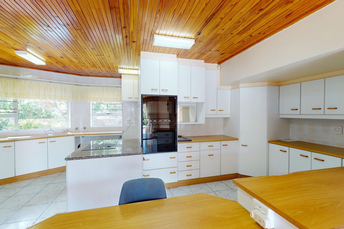 Spacious kitchen featuring white cabinetry, laminate countertops, a built-in oven, and a distinctive timber-paneled ceiling with tiled flooring.