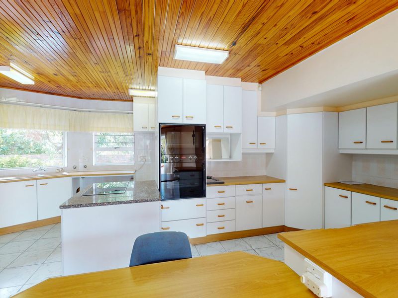 Spacious kitchen featuring white cabinetry, laminate countertops, a built-in oven, and a distinctive timber-paneled ceiling with tiled flooring.