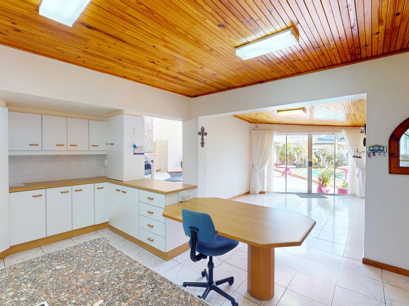 Open-plan kitchen and living area featuring timber ceilings, tiled floors, and direct access to the outdoor pool area through sliding glass doors.