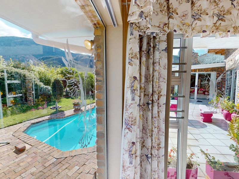 View from an interior space looking out onto a paved patio area with a swimming pool and landscaped garden.