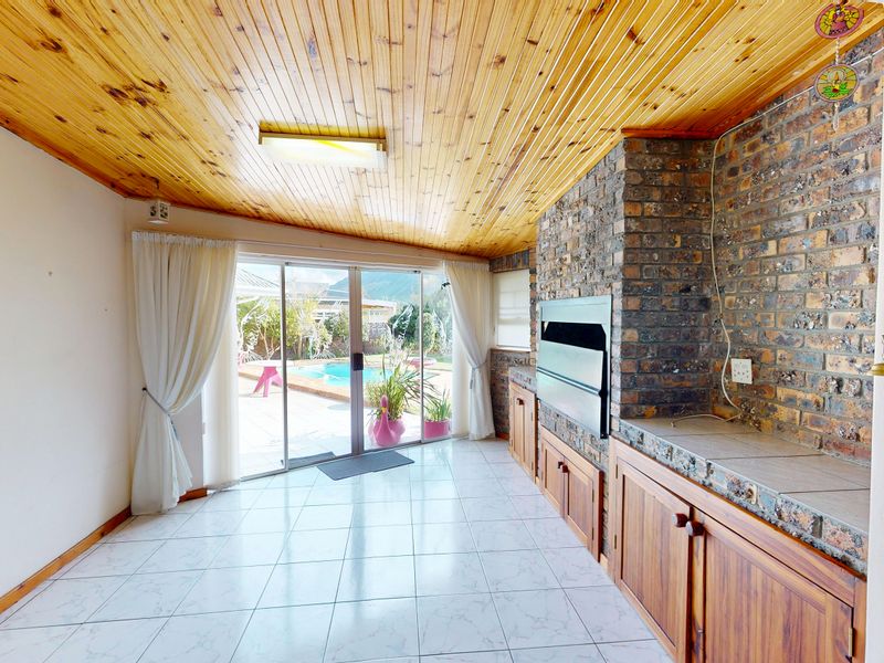 Covered patio area featuring a built-in braai, timber ceiling, and direct access to the pool area through sliding glass doors.