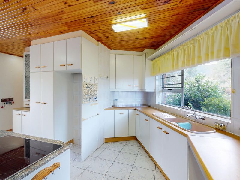 A functional kitchen featuring white cabinetry, timber ceiling, and an electric hob, offering a classic layout with potential for modern updates.