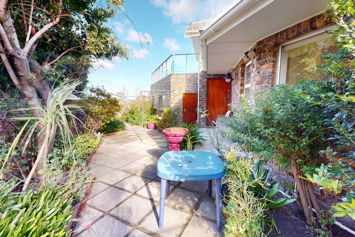 A rear exterior view featuring a paved patio area, brick facade, and an elevated balcony with a glass balustrade.