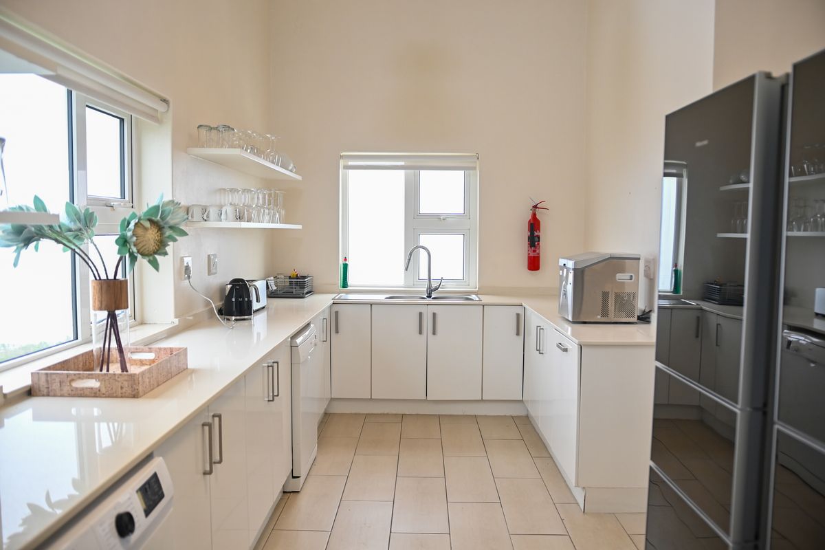 A clean, modern kitchen featuring white cabinetry, stone countertops, stainless steel sink, and tiled flooring with ample natural light.