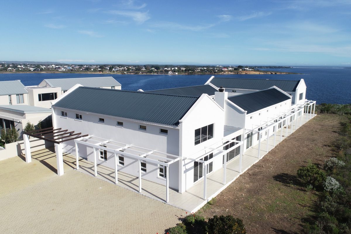 Aerial view of a modern coastal residence featuring a white facade, dark metal roofing, and extensive pergola structures overlooking the ocean.