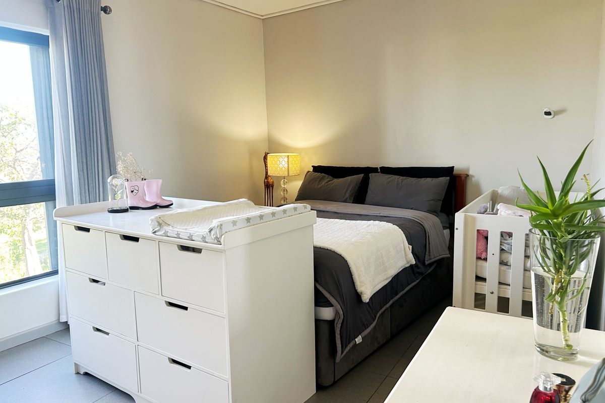 A well-lit bedroom featuring tiled flooring and a large window, currently configured as a nursery with ample space for bedroom furniture.
