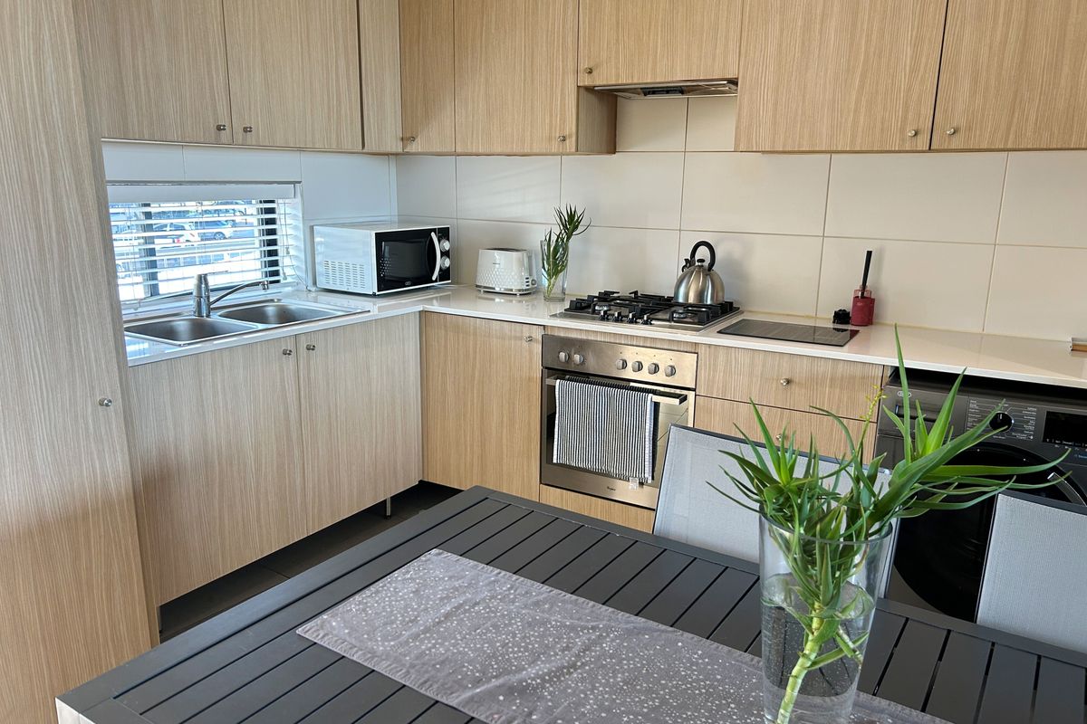Modern kitchen featuring light wood-grain cabinetry, stone countertops, integrated gas hob, built-in oven, and a double sink with tiled splashback.