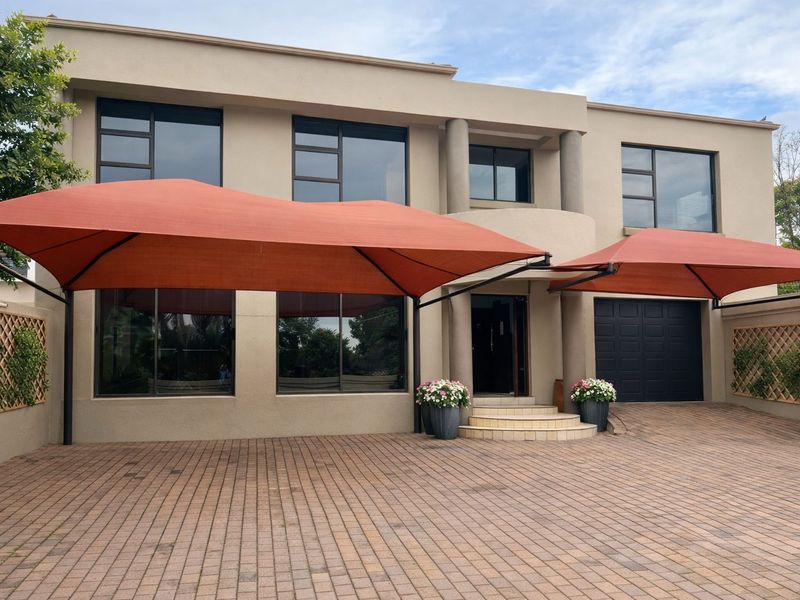 Front elevation of a modern apartment building featuring a paved driveway, integrated garage, and large shade sails over the entrance area.