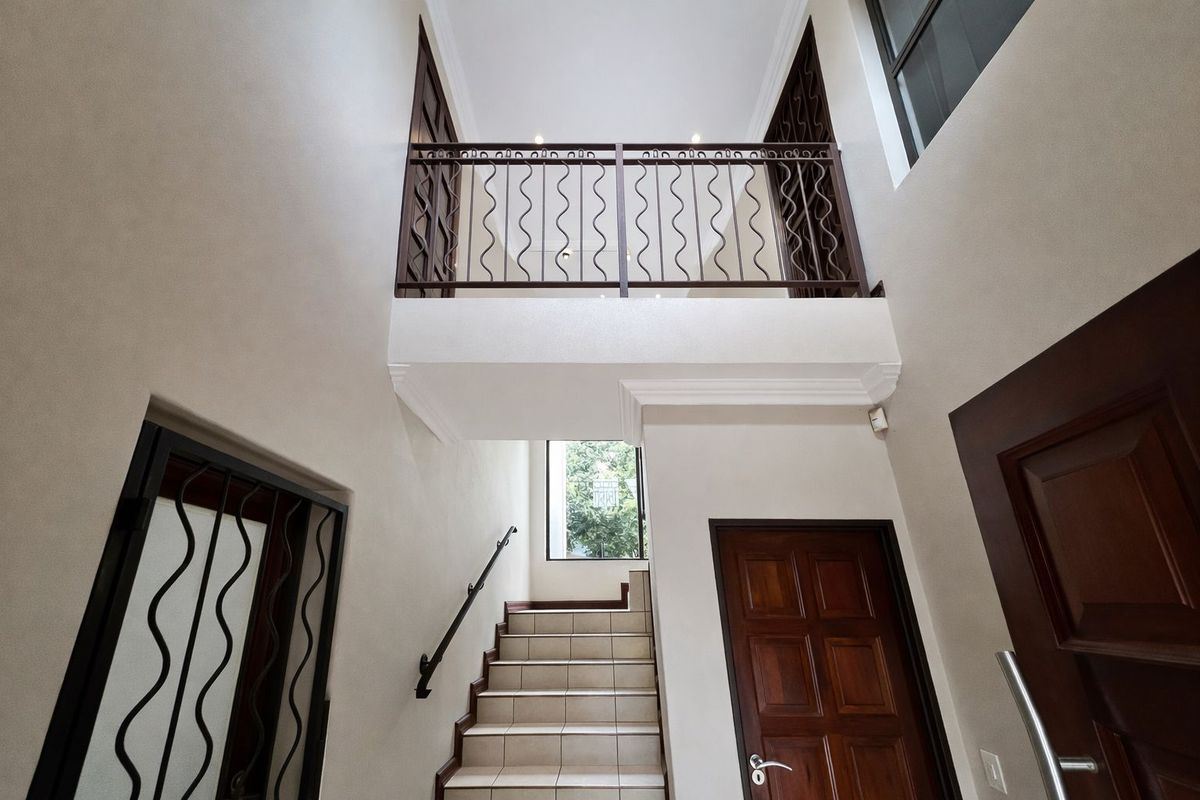 Spacious double-volume entrance hall featuring a tiled staircase with a decorative metal balustrade and solid wood doors.