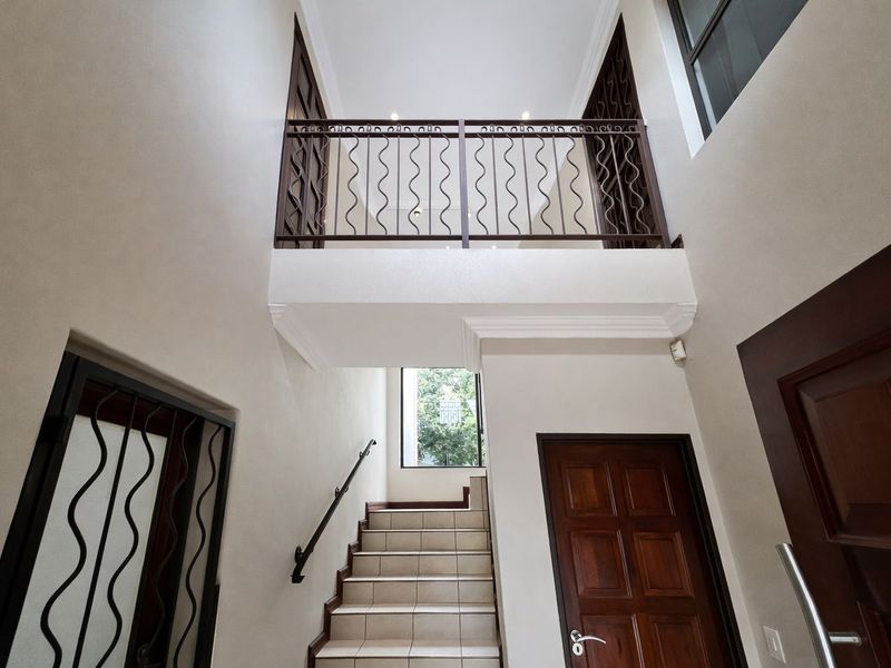Spacious double-volume entrance hall featuring a tiled staircase with a decorative metal balustrade and solid wood doors.