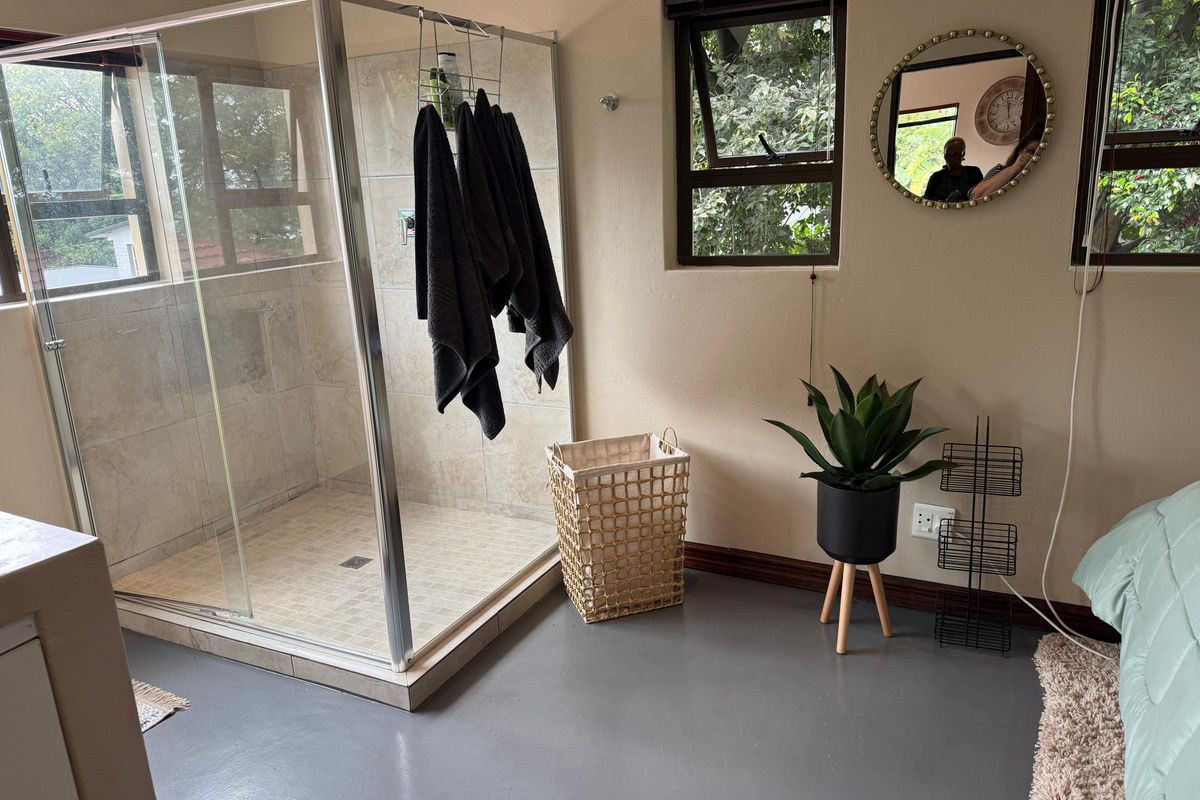 A bathroom featuring a glass-enclosed shower with tiled finishes, awning windows, and painted concrete flooring.