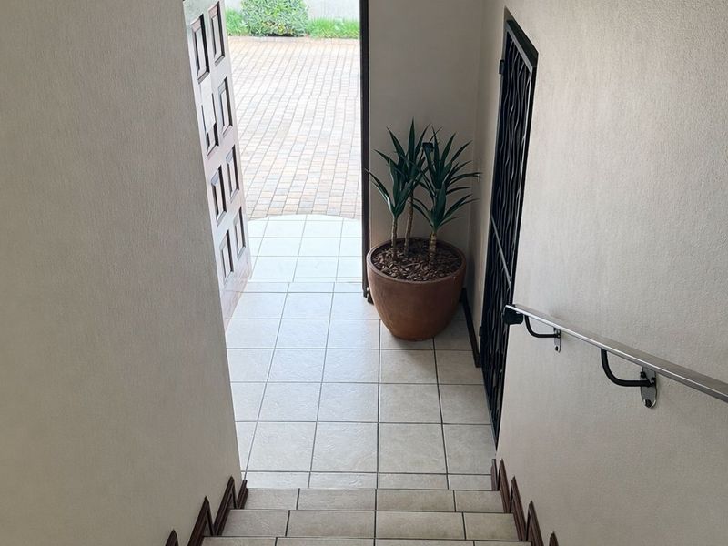 An entryway featuring a tiled staircase with a metal handrail, leading to an exterior door with a security gate.