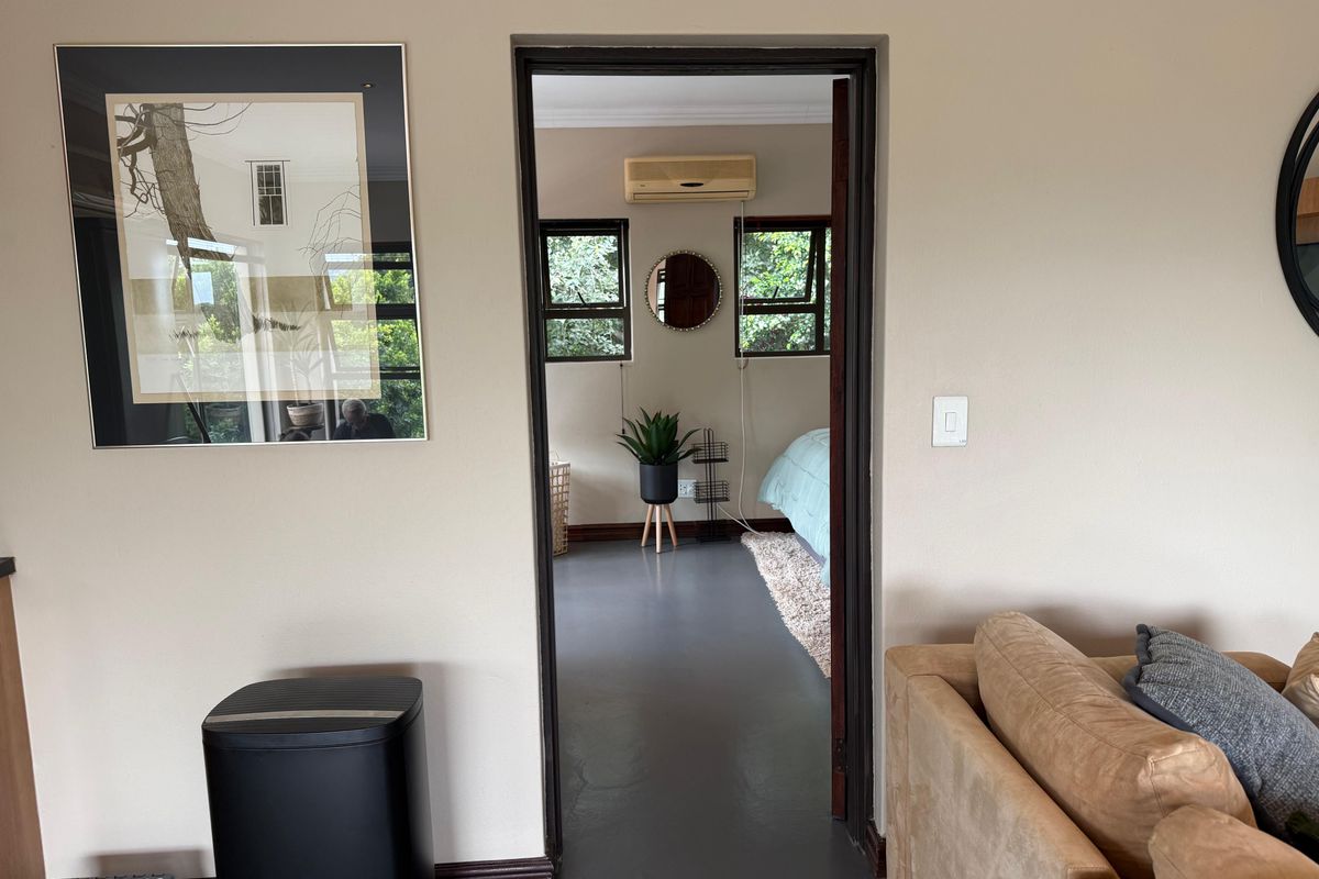 A view through a doorway into a bedroom featuring painted concrete floors, casement windows, and a wall-mounted air conditioning unit.
