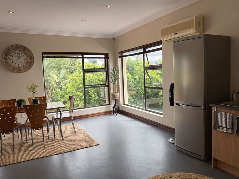 Open-plan living and dining area featuring large windows with garden views, recessed lighting, and integrated kitchen cabinetry with a stainless steel sink.