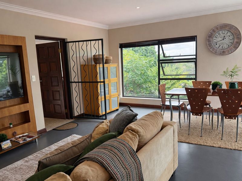 Spacious open-plan living and dining area featuring modern flooring, built-in media cabinetry, and large windows with natural light and garden views.