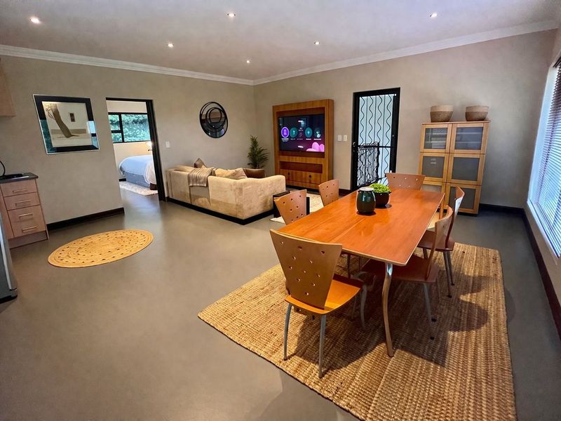 Spacious open-plan living and dining area featuring polished concrete floors, recessed lighting, and a built-in media unit, with seamless flow to the bedroom.