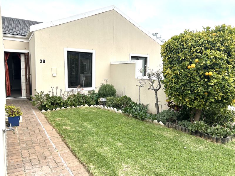 A well-maintained front exterior view of the property featuring a paved walkway, neat lawn, and established garden beds leading to the main entrance.