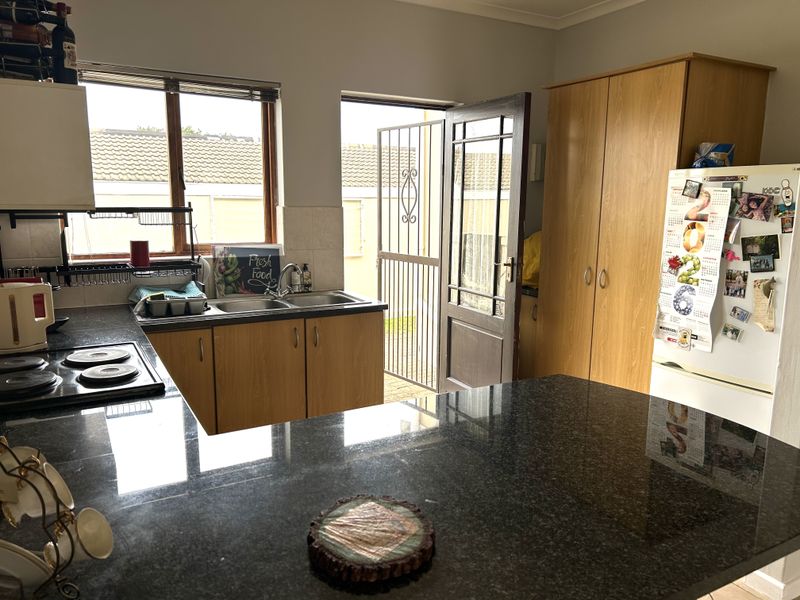 A functional kitchen featuring granite countertops, built-in wooden cabinetry, an electric hob, and direct access to the exterior via a security gate.