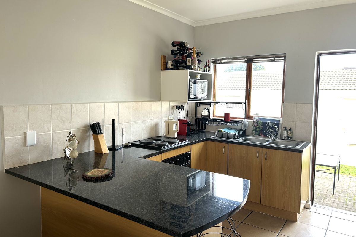 A functional kitchen featuring laminate cabinetry, dark granite countertops, an electric hob, built-in oven, and a double basin sink with direct access to the rear patio.