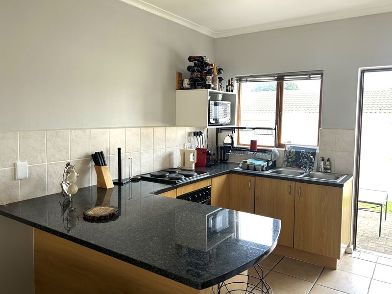 A functional kitchen featuring laminate cabinetry, dark granite countertops, an electric hob, built-in oven, and a double basin sink with direct access to the rear patio.