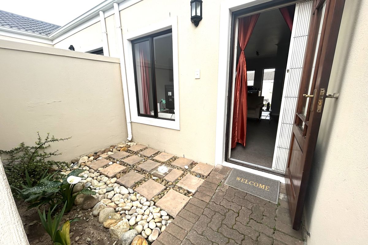 A small, low-maintenance rear courtyard featuring a paved patio area, pebble landscaping, and direct access to the interior living space.