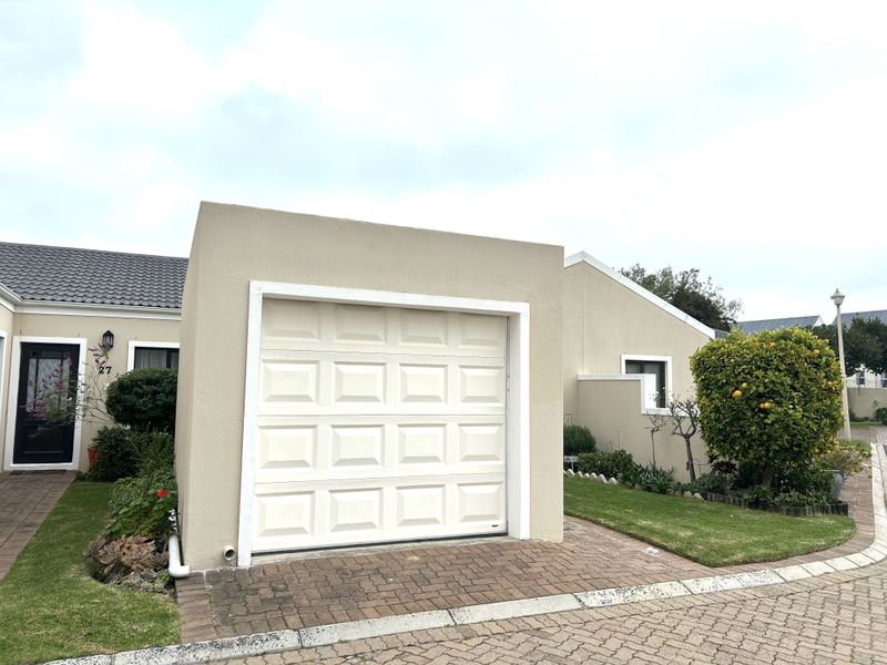 Front view of the property featuring a single garage, paved driveway, and well-maintained garden area.