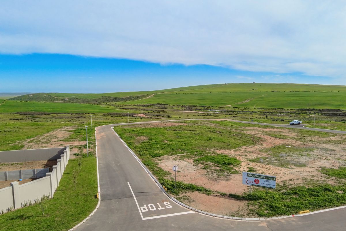 Aerial view of a vacant residential plot in a developed estate, featuring paved roads, boundary walls, and scenic landscape views.